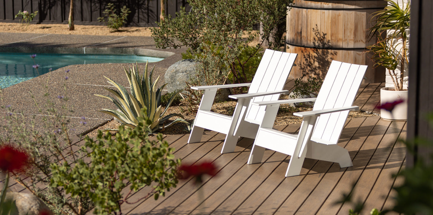 four white adirondack chairs in a row, sitting next to a gravel bocce court with bocce balls scattered about.