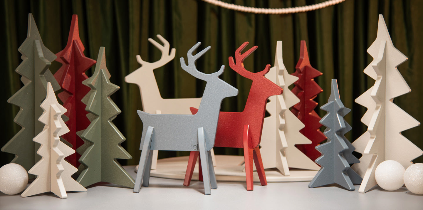 holiday decor of large and small reindeer and trees setup in a studio scene surrounded by pine christmas tress with a sofa cocktail table and lounge chair sitting on an area rug