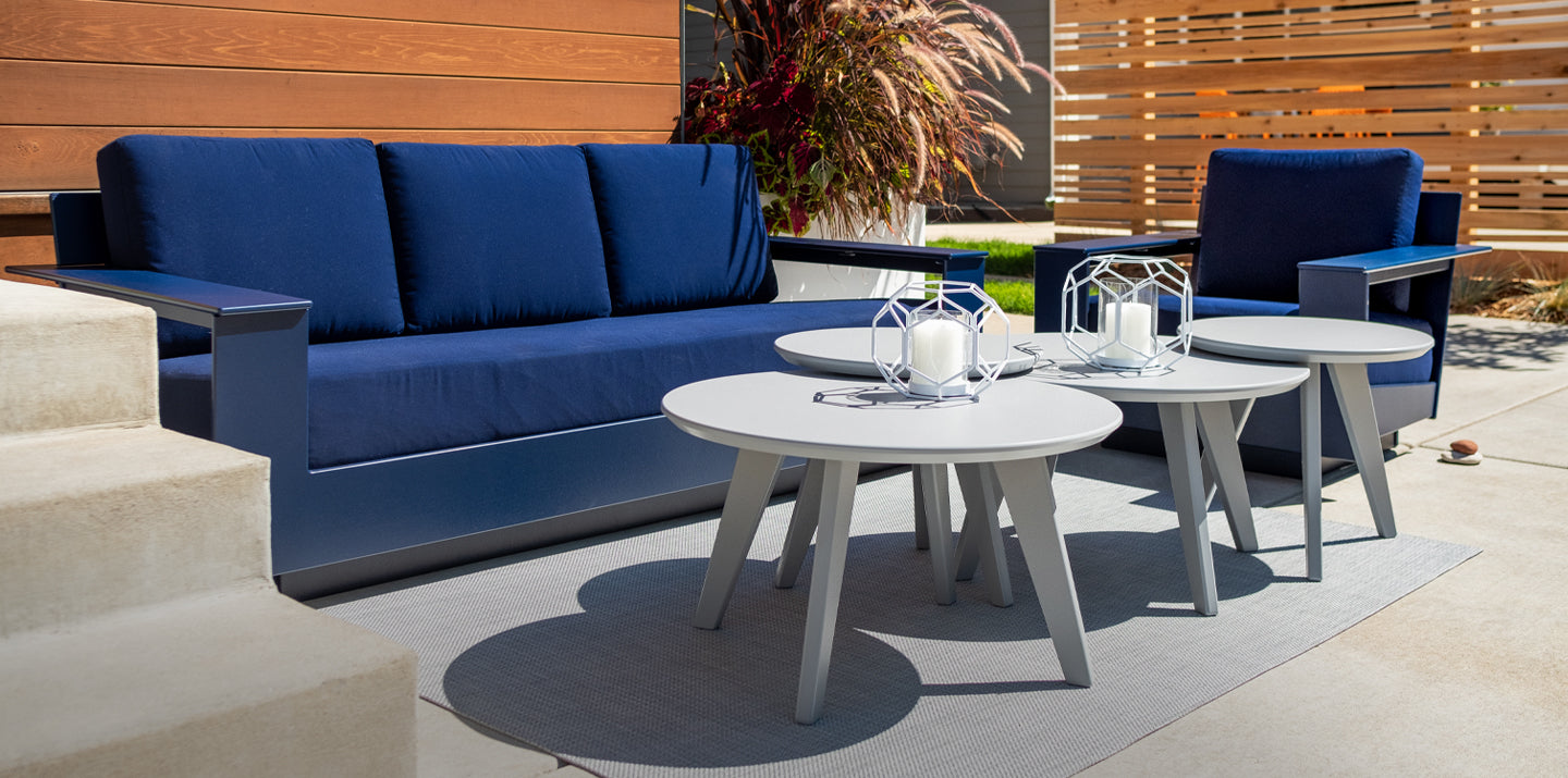 A Nisswa Couch and Lounge Chair in Navy blue with navy cushions. in front of the soft seating pieces are four different satellite tables in driftwood. 